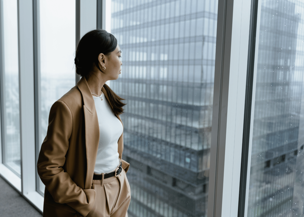 Woman looking out office window in city, thinking about trauma and the nervous system.