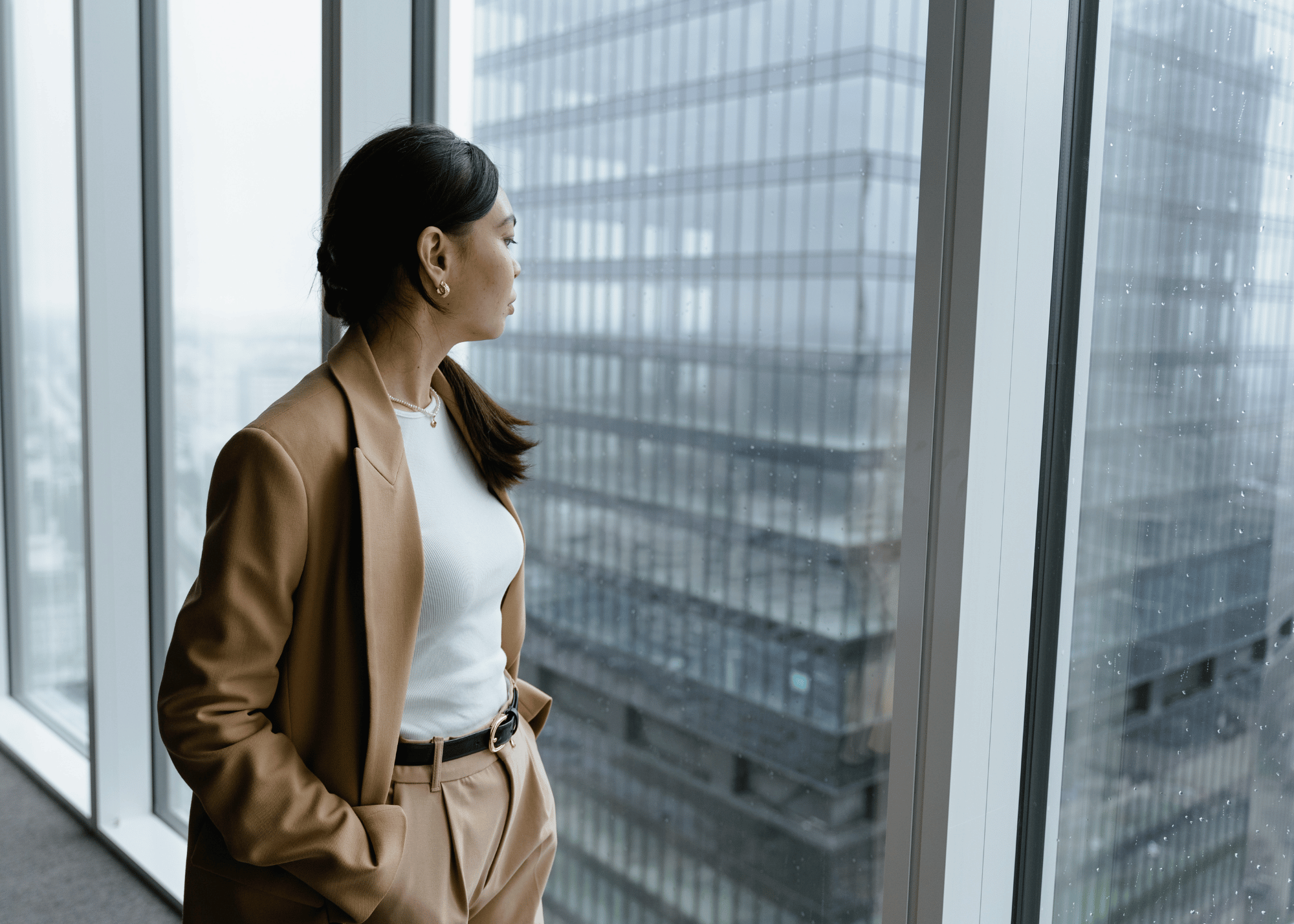 Woman looking out office window in city, thinking about trauma and the nervous system.