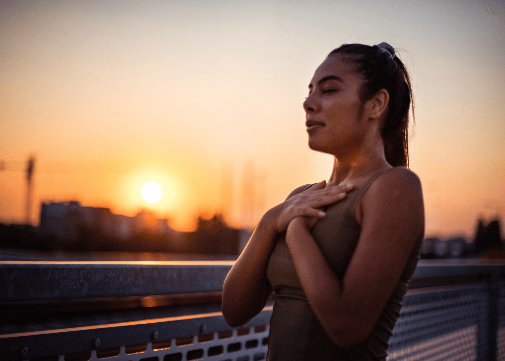 A person standing outside at sunset with their hands over their hearts, while practicing somatic exercises for burnout.